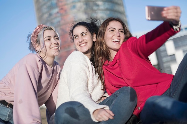 Amici donne felici che si fanno un selfie mentre sono sedute sulla terrazza di un edificio contro il cielo