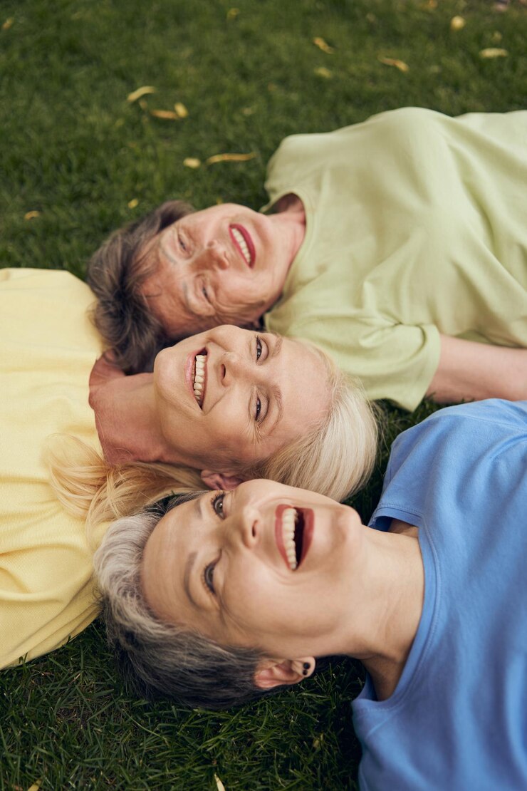 Amici donne mature sdraiate testa a testa sull'erba stanno ridendo e divertendosi insieme