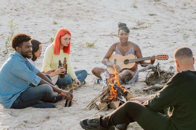 Amici falò all'aperto all'aperto bella ragazza dalla pelle scura che suona la chitarra