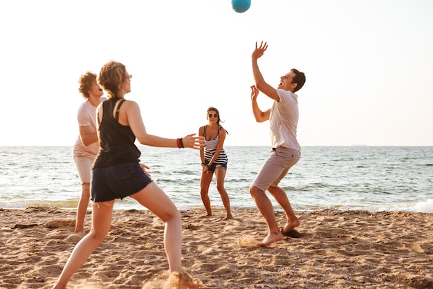 Amici felici all'aperto sulla spiaggia giocano a pallavolo divertendosi