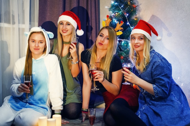 Amici felici che festeggiano il Natale o il nuovo anno con un bicchiere di champagne e brindando. Cinque belle ragazze che festeggiano il natale a casa