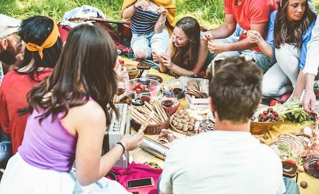 Amici felici che mangiano e che bevono vino al picnic all'aperto