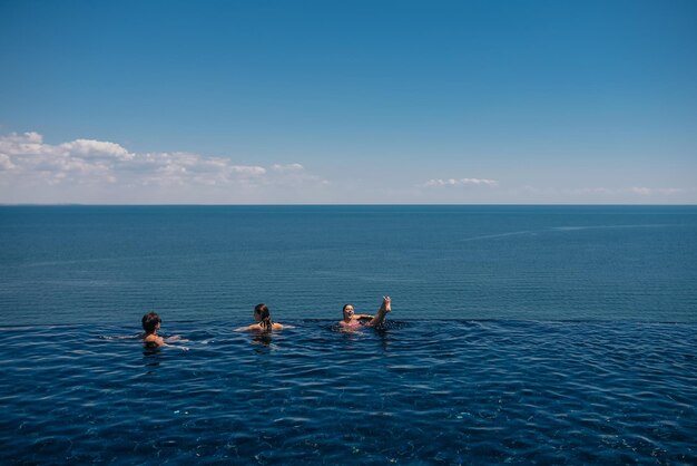 Amici felici che nuotano nella piscina a sfioro contro il lungomare