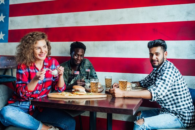 amici felici che riposano insieme al bar, donne e uomini al bar, parlando, ridendo mangiano fast food.