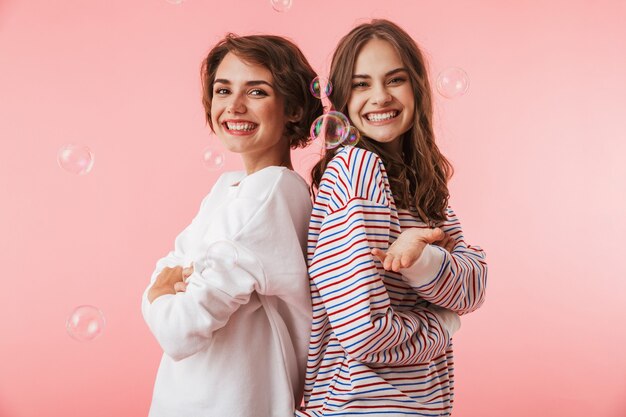 Amici felici delle donne isolate sopra la parete rosa sopra le bolle di sapone.