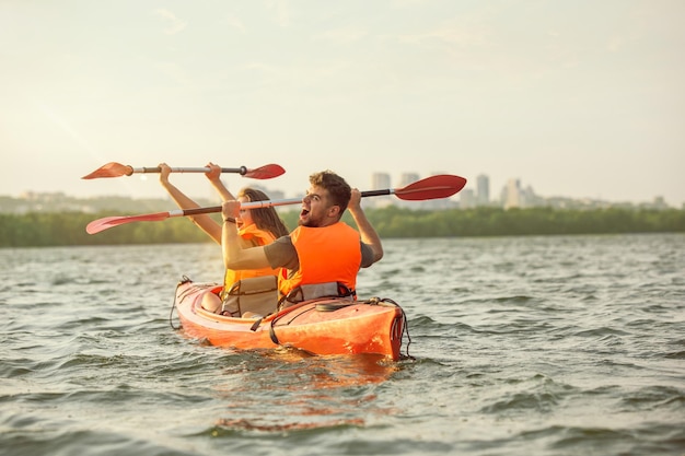 Amici felici in kayak sul fiume con il tramonto sullo sfondo