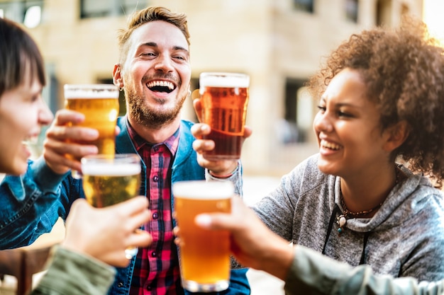 Amici felici multiculturali che bevono e tostano birra al ristorante del bar della birreria