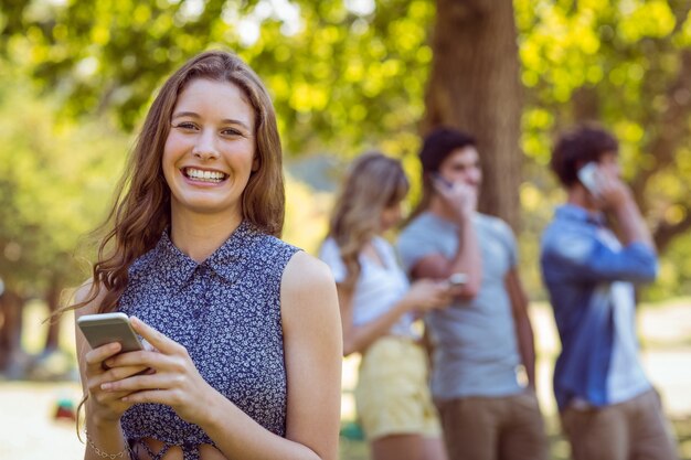 Amici felici nel parco usando i loro telefoni