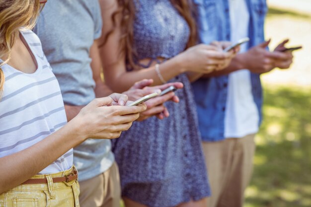 Amici felici nel parco usando i loro telefoni