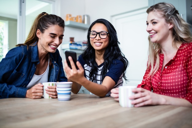 Amici femminili allegri che per mezzo del telefono cellulare dalla tavola a casa