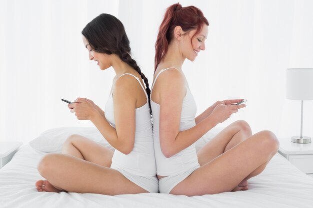 Amici femminili che si siedono back-to-back e messaggi di testo sul letto