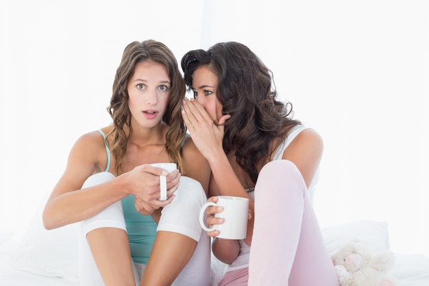 Amici femminili con le tazze di caffè che pettegolano a letto