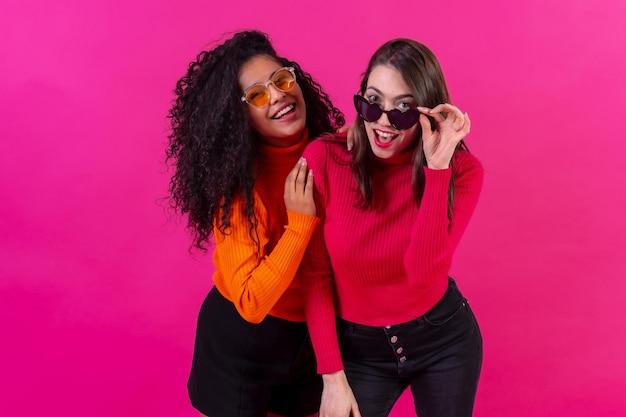 Amici femminili in occhiali da sole che si divertono con sfondo rosa girato in studio