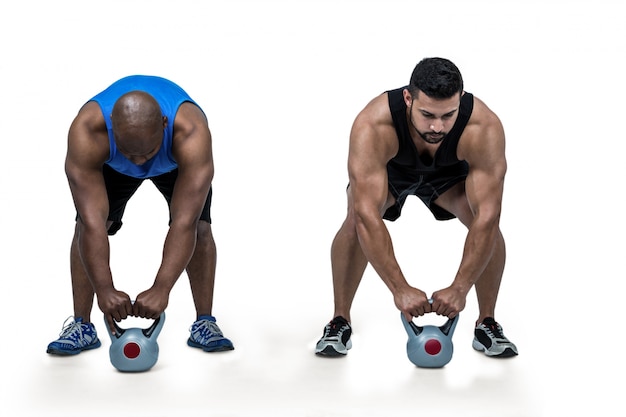 Amici forti che sollevano insieme i kettlebells