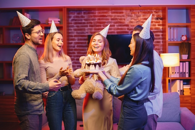 Amici in piedi insieme tenendo un piatto con una torta e festeggiando il compleanno