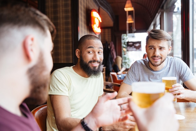 Amici maschi sorridenti che parlano e bevono birra in pub