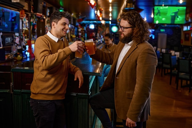 Amici maschii felici che clinking con le tazze di birra in pub