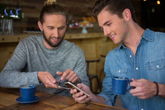 Amici maschii felici utilizzando smart phone al tavolo in casa di caffè