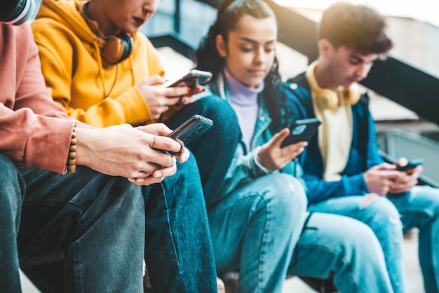 Amici millenari che guardano dispositivi mobili intelligenti all'esterno Giovani che usano telefoni cellulari giocando su piattaforme di social media Concetto di dipendenza dalla tecnologia
