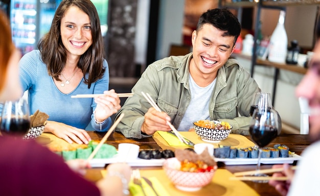 Amici multiculturali della generazione z che mangiano sushi con le bacchette nella cantina del ristorante fusion