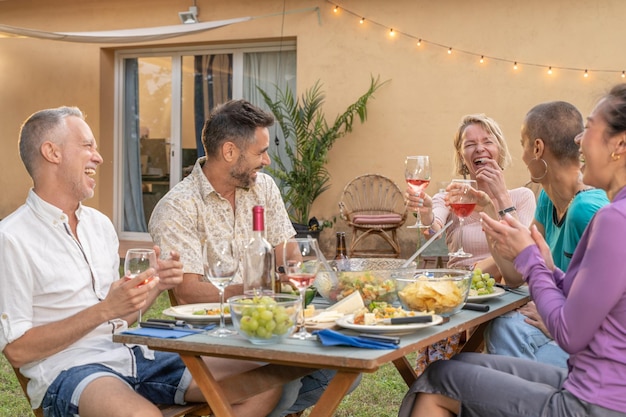 Amici multietnici che mangiano e bevono felici sorridendo e ridendo nel patio