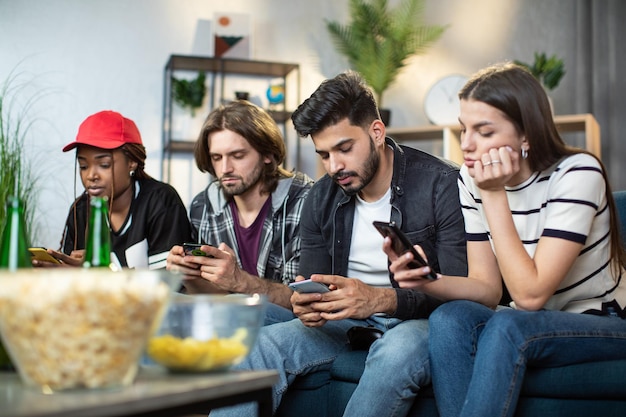 Amici multietnici che utilizzano smartphone personali sul divano