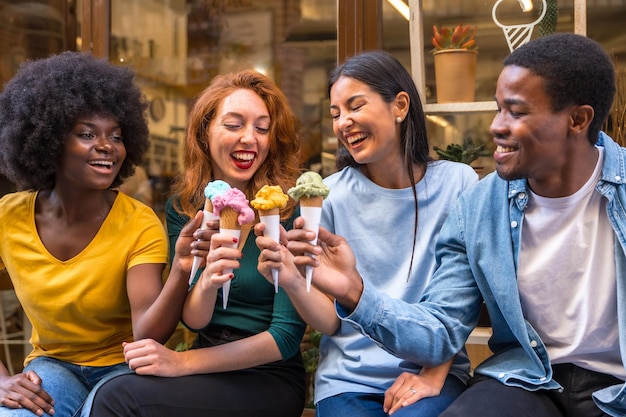 Amici multietnici in una gelateria seduti a mangiare un gelato estivo sfoggiando i gelati