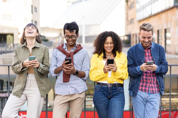 Amici multirazziali che ridono utilizzando lo smartphone nel quartiere universitario della città Giovani dipendenti dagli smartphone mobili Concetto tecnologico con gen z e millennial sempre connessi