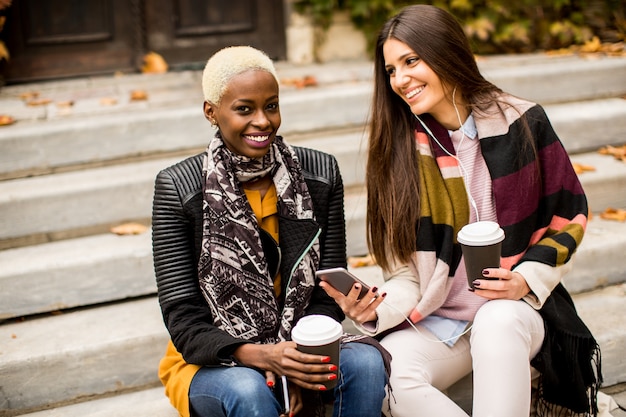 Amici multirazziali seduti nel parco d&#39;autunno, parlando e portare il caffè per andare nelle mani