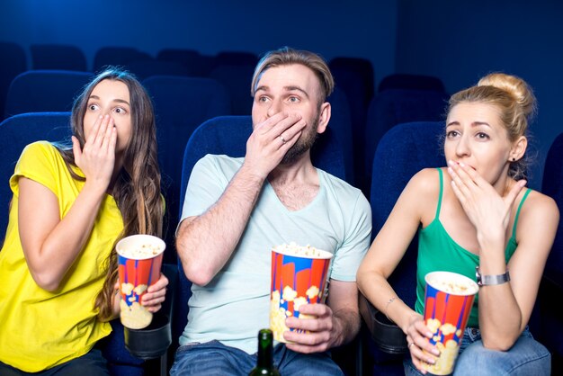 Amici scioccati che guardano film seduti insieme a popcorn al cinema