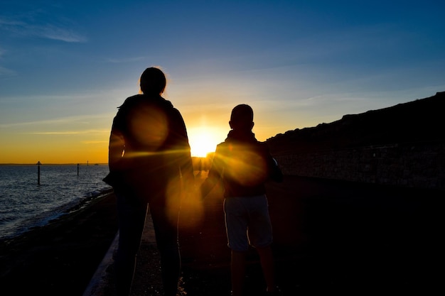 Amici silhouette in piedi sulla riva contro il cielo durante il tramonto