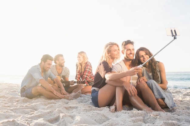 Amici sorridenti che si siedono sulla sabbia che canta e che prende i selfie