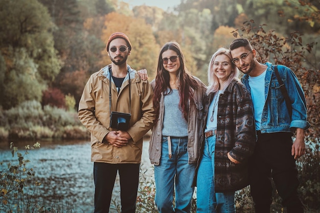 Amici sorridenti felici che si godono la passeggiata autunnale, circondati da alberi e fiume.