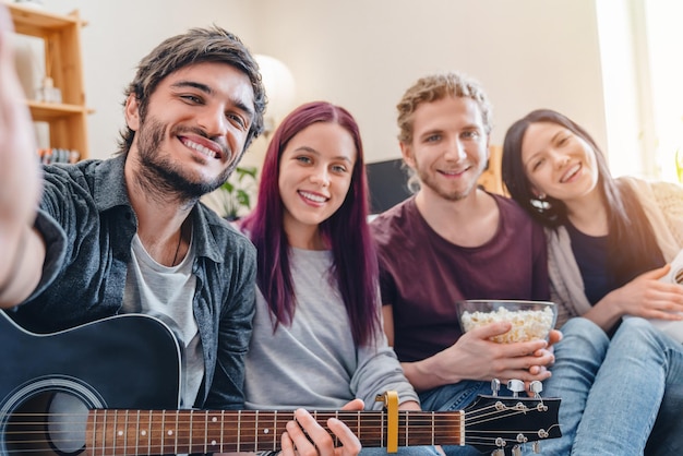 Amici sorridenti in casual sul divano a casa con la chitarra che fa selfie