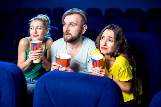 Amici spaventati che guardano film seduti insieme a popcorn al cinema