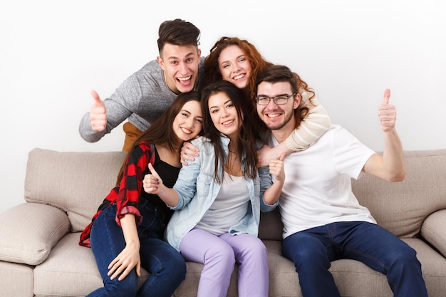 Amici studenti felici che si divertono, si fanno selfie e posano davanti alla telecamera, seduti sul divano in casa