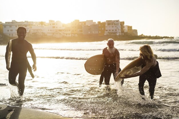 Amici surfisti multigenerazionali che si divertono mentre navigano sulla spiaggia - Soft focus sull'uomo giusto