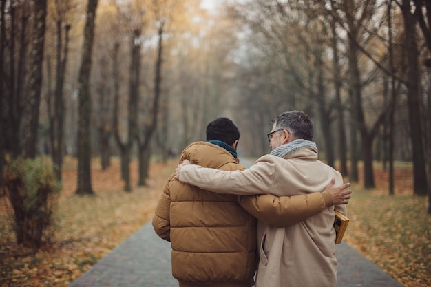 Amici un anziano e un giovane che camminano, parlano e bevono caffè insieme nel parkxA autunnale