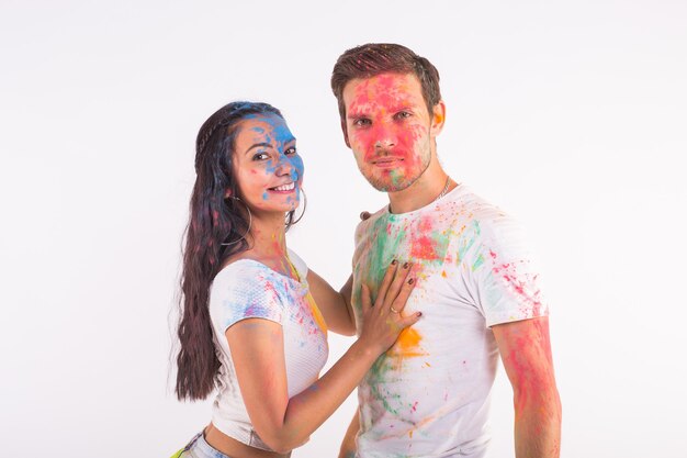 Amicizia, amore, festival di holi, concetto di persone - giovani coppie che giocano con i colori al festival di holi su superficie bianca