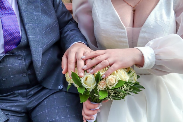 Amicizia e connessioni Gli sposi si tengono per mano Mani grassocce della sposa e dello sposo con fedi nuziali e un bouquet Primo piano