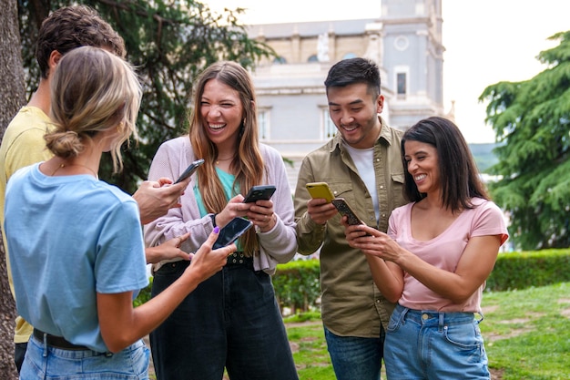 Amicizia multiculturale Cinque giovani amici impegnati con i telefoni cellulari in un parco della città