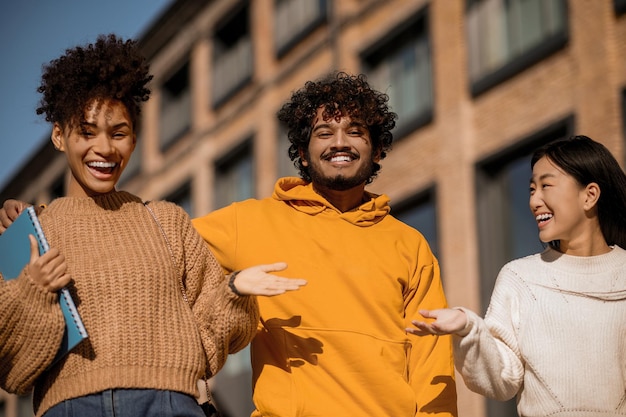 Amicizia. Ragazzo sorridente indiano baffuto in felpa gialla che guarda l'obbiettivo e ragazze asiatiche e mulatte che ridono gesticolando sulla strada della città in una giornata di sole