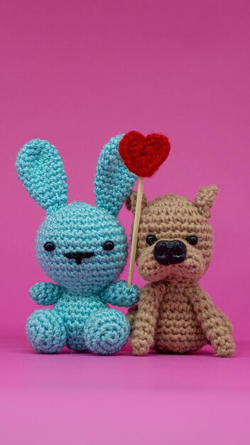 Amigurumi di coniglio e cane con cuore, su sfondo verticale rosa.