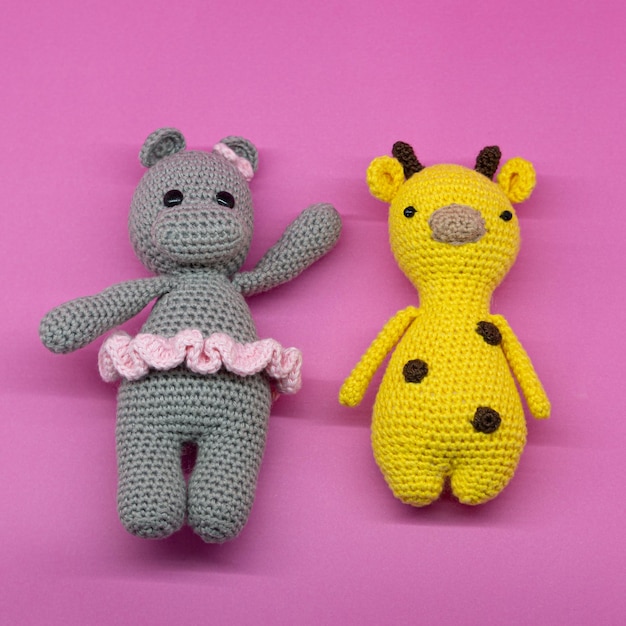 Amigurumi di ippopotamo con tutù e giraffa a macchie marroni, su sfondo rosa.