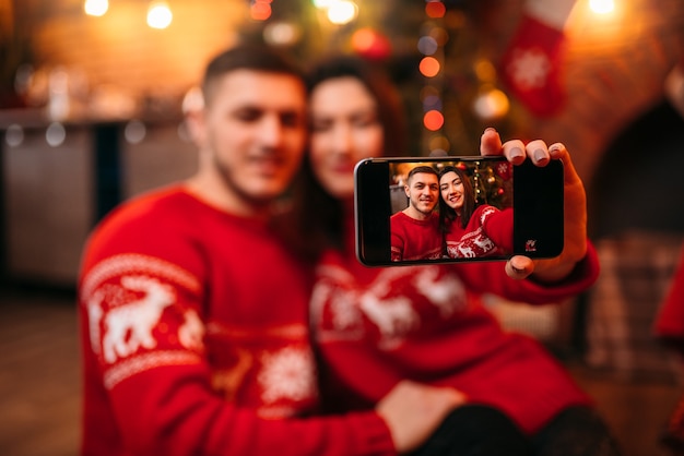 Amore coppia fa selfie sulla fotocamera del telefono, romantica celebrazione di Natale. Vacanze di Natale, uomo e donna felici insieme, decorazioni festive