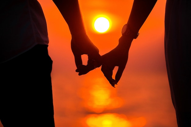 Amore - coppie romantiche che si tengono per mano, tramonto della spiaggia. Amanti o sposini sposati giovane coppia in romanticismo sul bellissimo tramonto in spiaggia. Giovane donna e uomo innamorato che camminano mano nella mano sulla spiaggia.