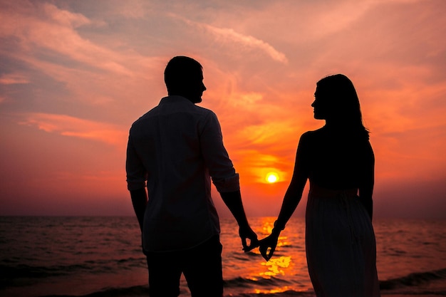 Amore - coppie romantiche che si tengono per mano, tramonto della spiaggia. Amanti o sposini sposati giovane coppia in romanticismo sul bellissimo tramonto in spiaggia. Giovane donna e uomo innamorato che camminano mano nella mano sulla spiaggia.