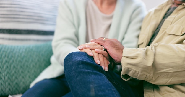 Amore da vicino e coppia anziana che si tengono per mano nel salotto di casa per il matrimonio insieme Sostenere il conforto e l'anziano uomo e donna con affetto per la relazione nel salotto della casa moderna