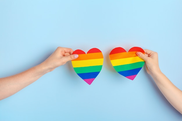 Amore gay. Mano umana che tiene un cuore di carta arcobaleno