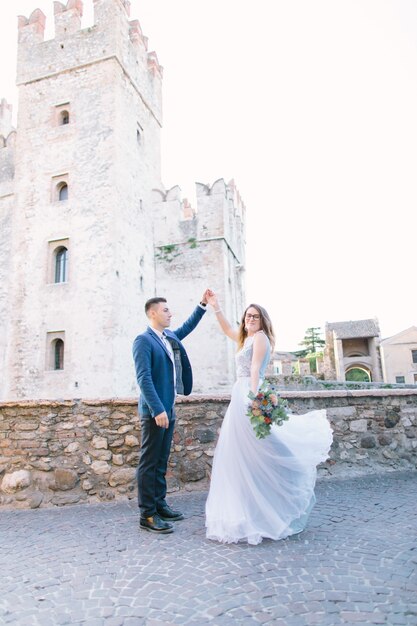 Amore in Italia, Sirmione. Bella coppia caucasica in abiti di lusso in posa vicino al Castello Scaligero (XIII secolo) a Sirmione sul lago di Garda vicino a Verona, Italia